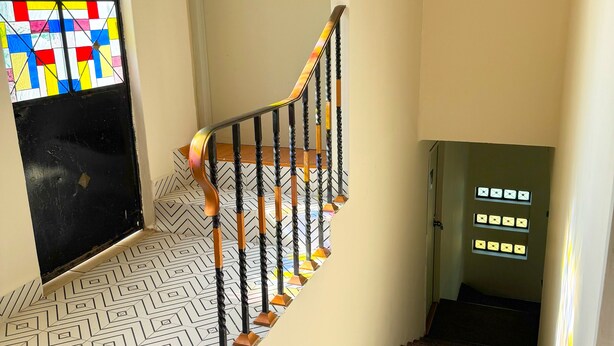 A staircase with a geometric patterned floor, a black and white railing, and a colorful stained glass window.