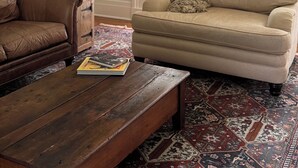 Un salon avec un canapé en cuir marron, un canapé beige agrémenté d’un plaid, une table basse en bois et un tapis à motifs.