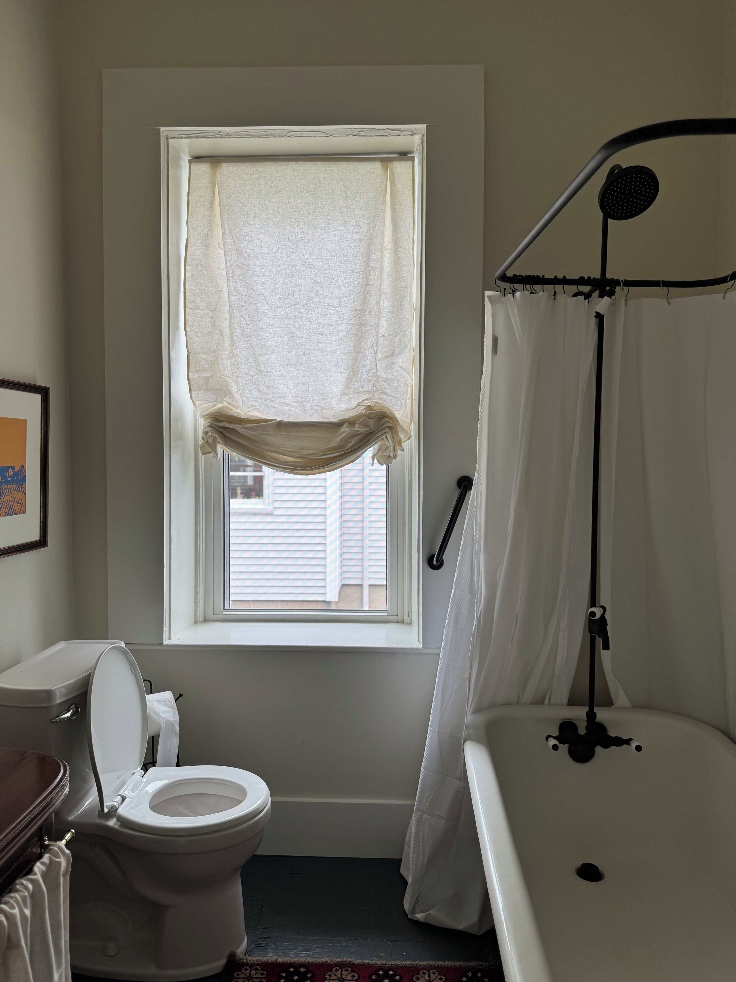 Ein Badezimmer mit Toilette, einem Fenster mit Vorhang und einer Badewanne mit Duschbrause.