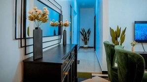Een moderne woonkamer met een donkerhouten console tafel, een groene fauteuil en een grote spiegel met bloemen in vazen.