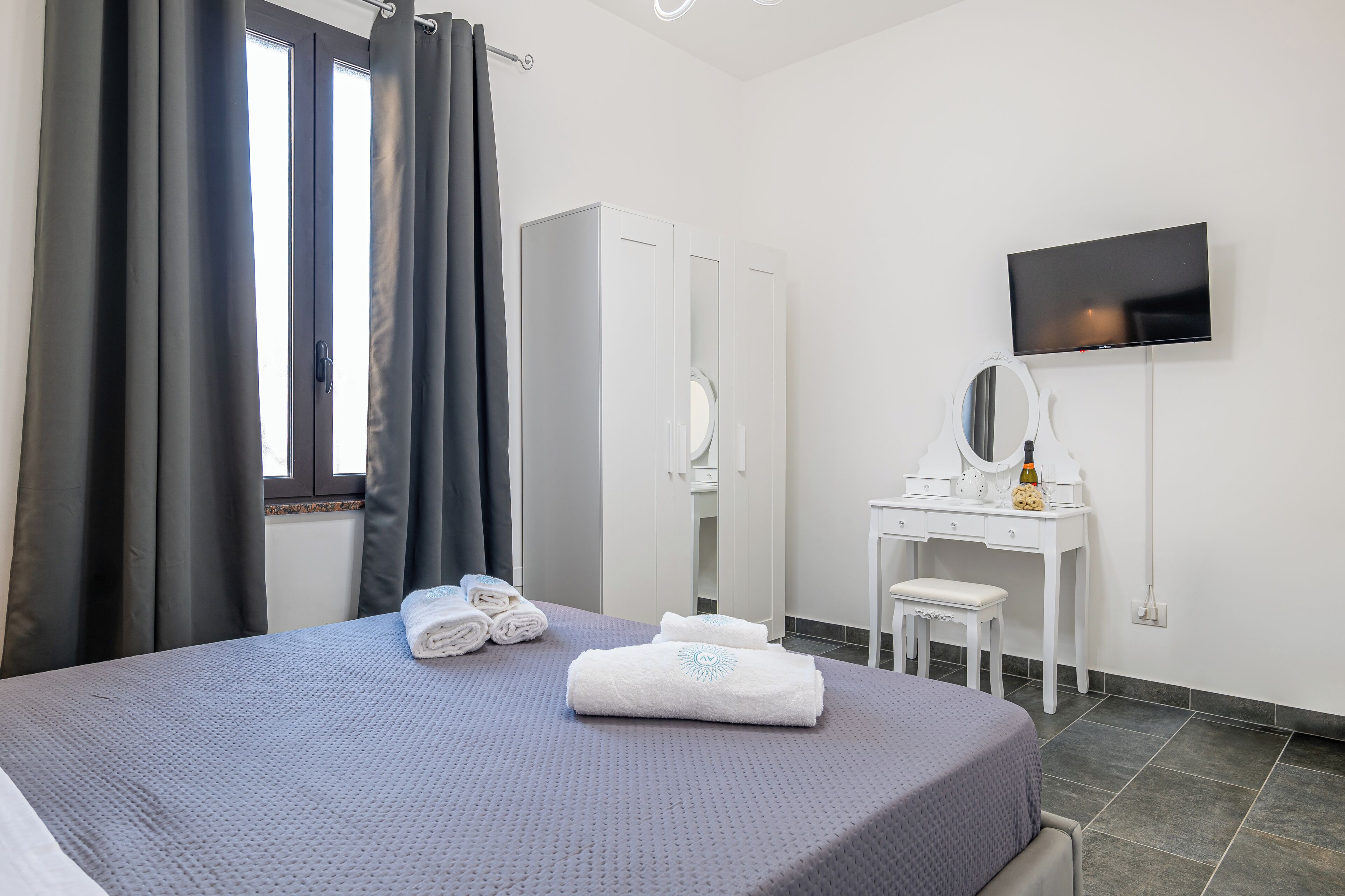 A hotel room with a bed, a desk, a mirror, and a TV on the wall.