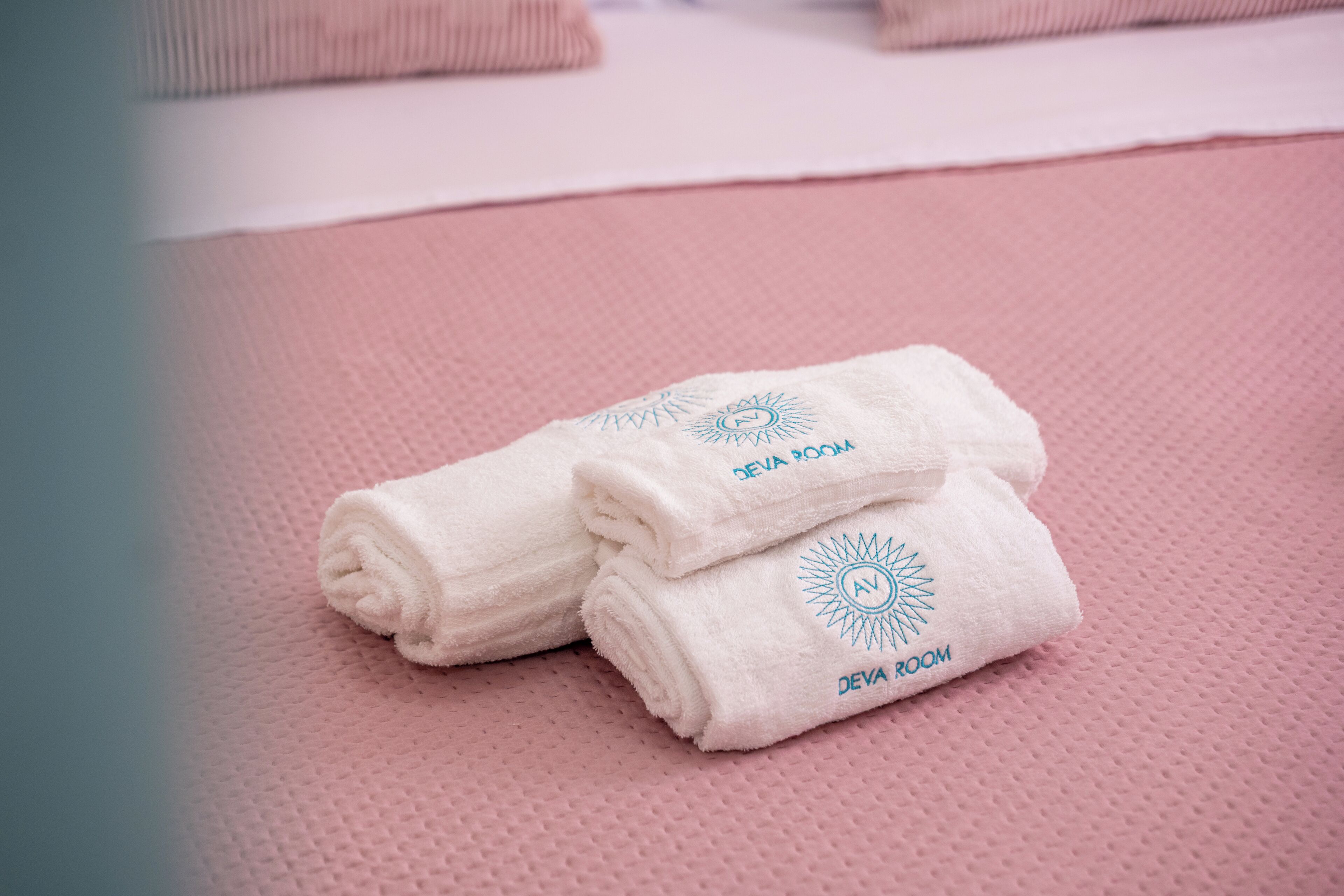 A stack of white towels with 'DEVA ROOM' branding on a pink textured surface.