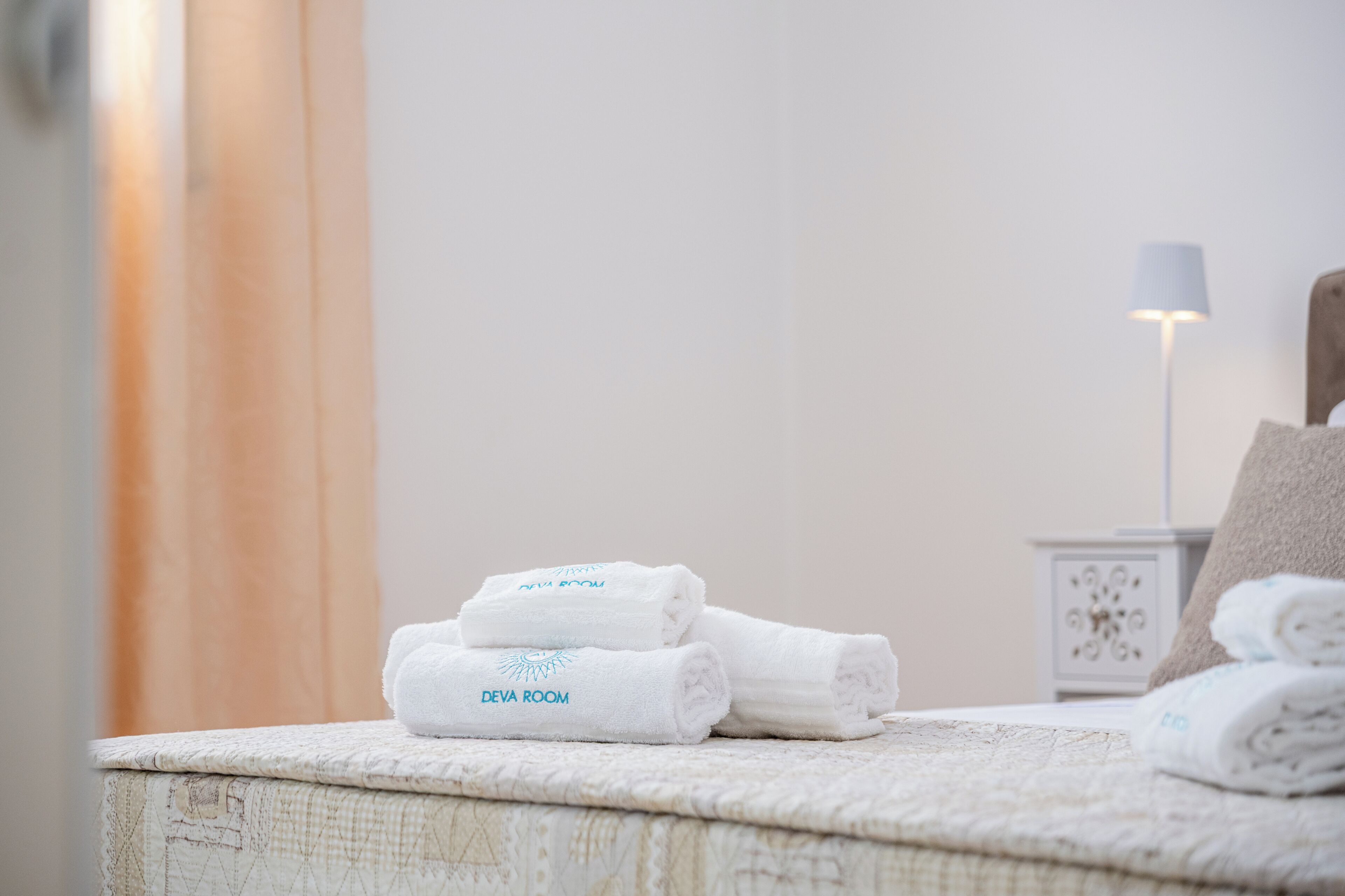 Ordentlich gefaltete Handtücher mit 'Deva Room'-Branding auf einem Bett in einem Hotelzimmer.