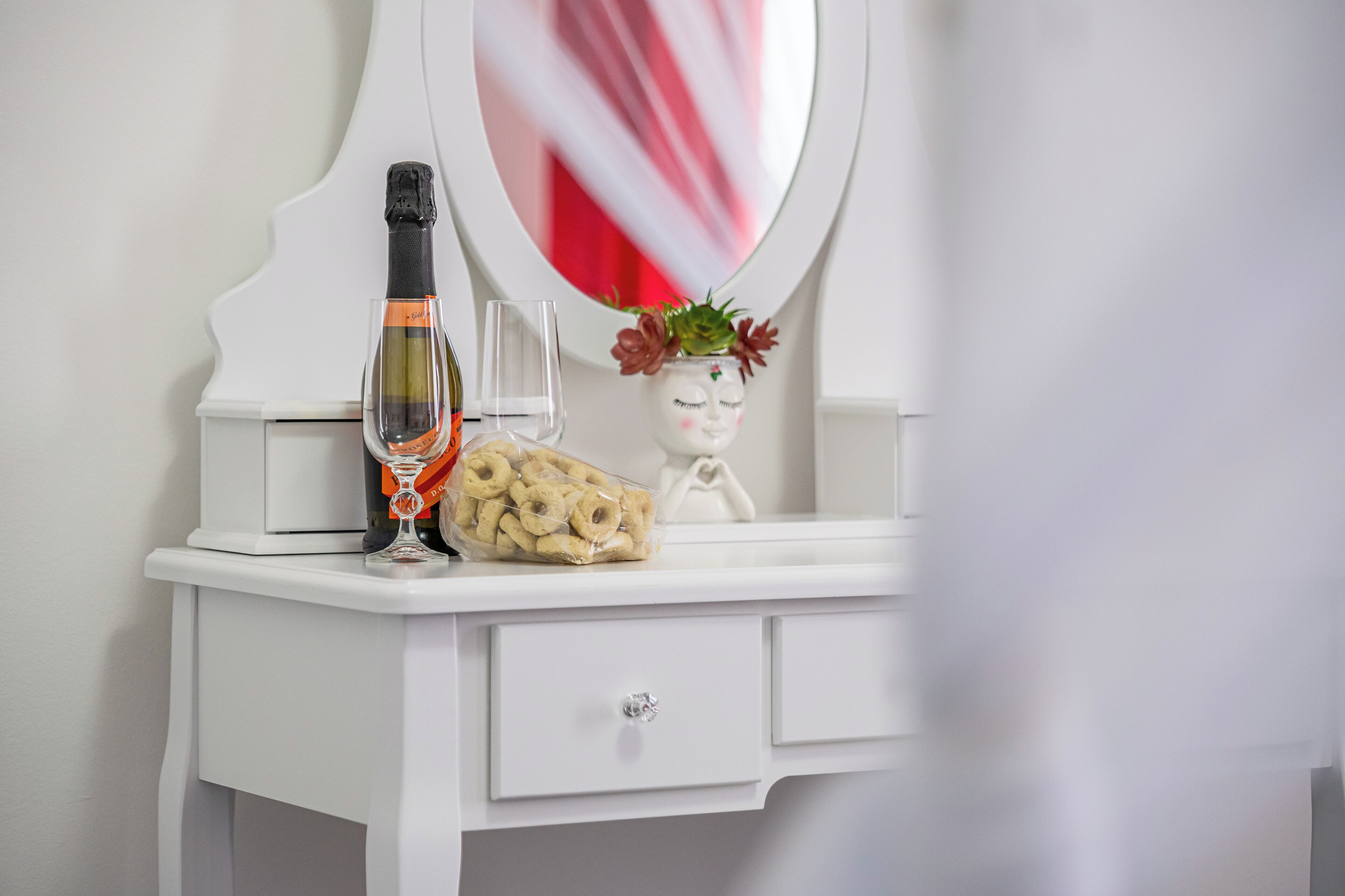 A white vanity with a bottle of champagne, a glass, and a decorative item with flowers.