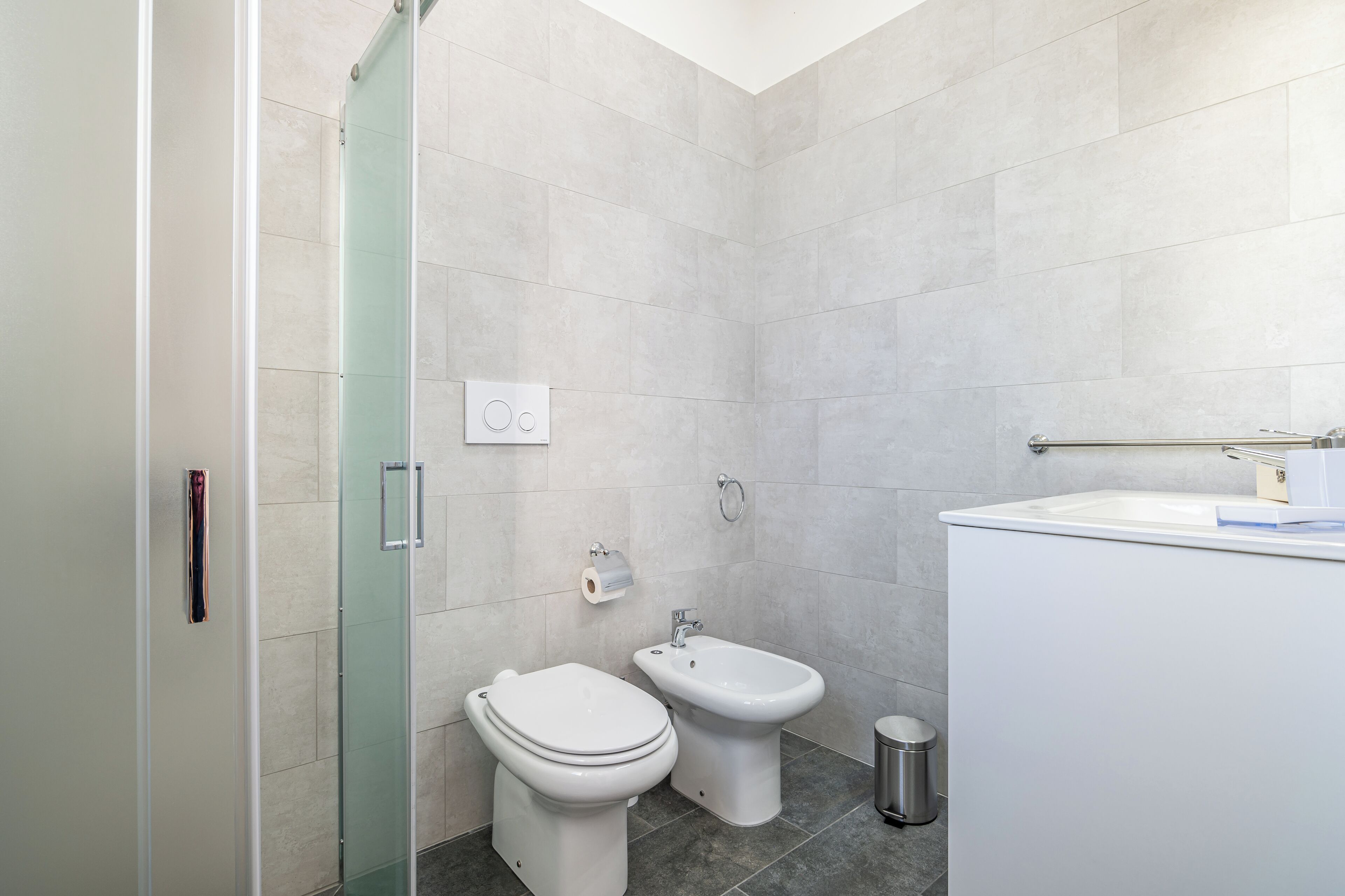 A modern bathroom with a toilet, bidet, and a glass shower enclosure.