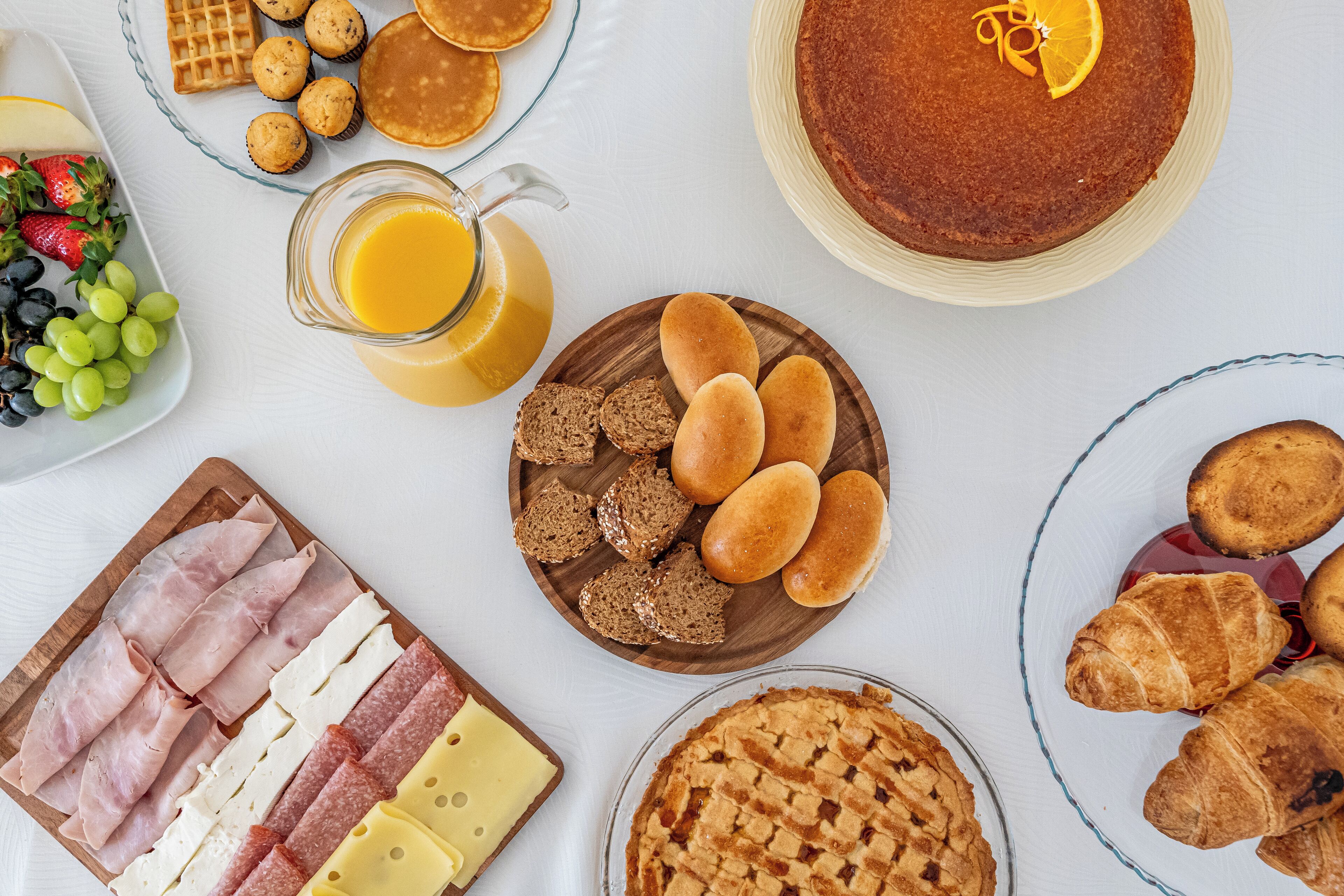 Una mesa de desayuno con una variedad de alimentos, como pasteles, pan, queso y una tarta.