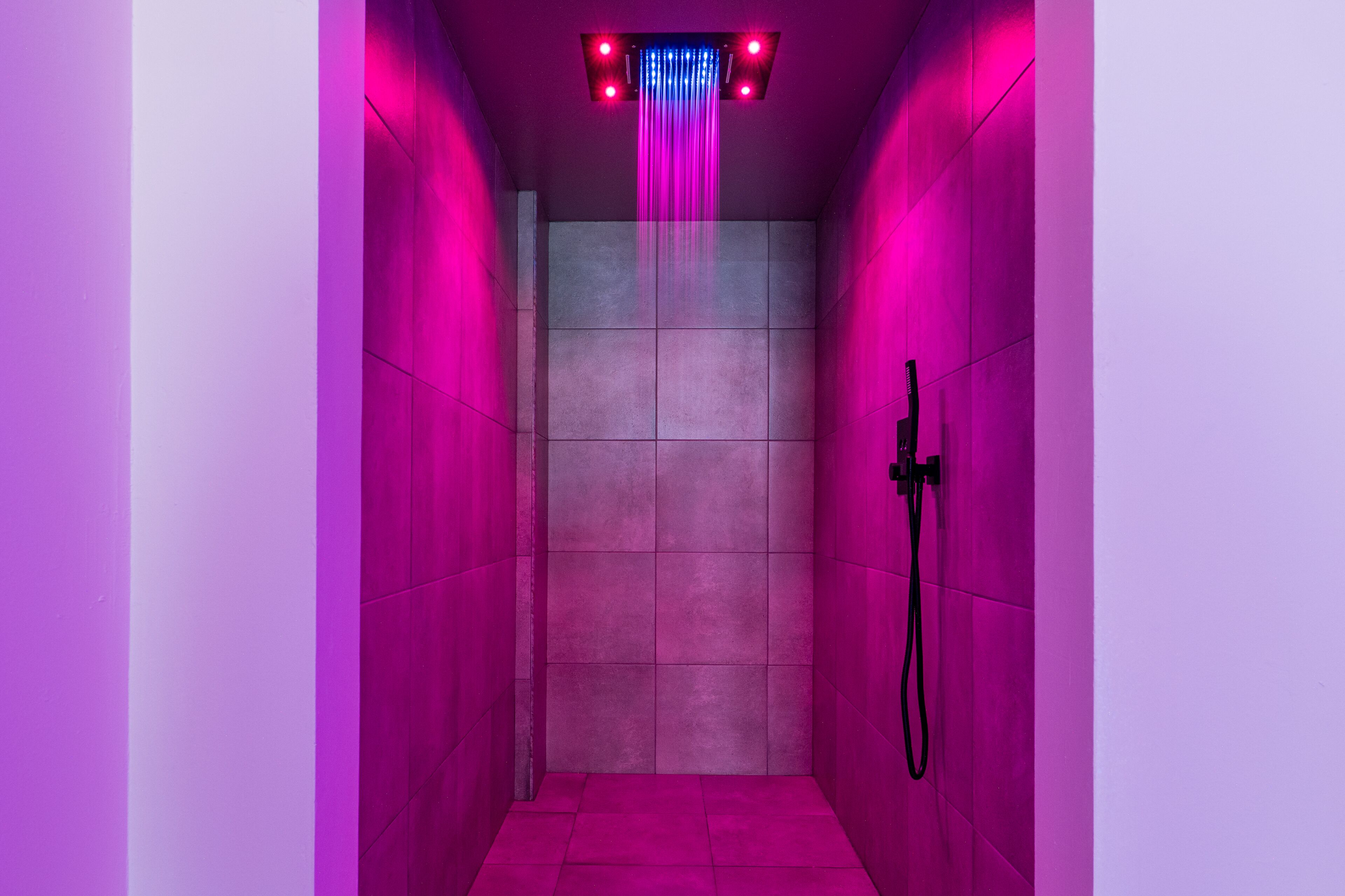 A narrow, tiled shower area with a handheld showerhead and a wall-mounted faucet.