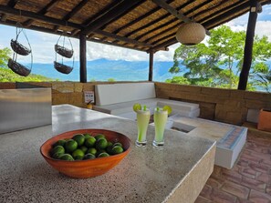 A covered outdoor seating area with a stone wall, a bowl of limes, and two glasses of a lime-based drink.