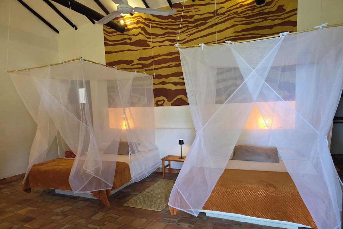 Two beds with mosquito nets, a patterned wall, and a ceiling fan.