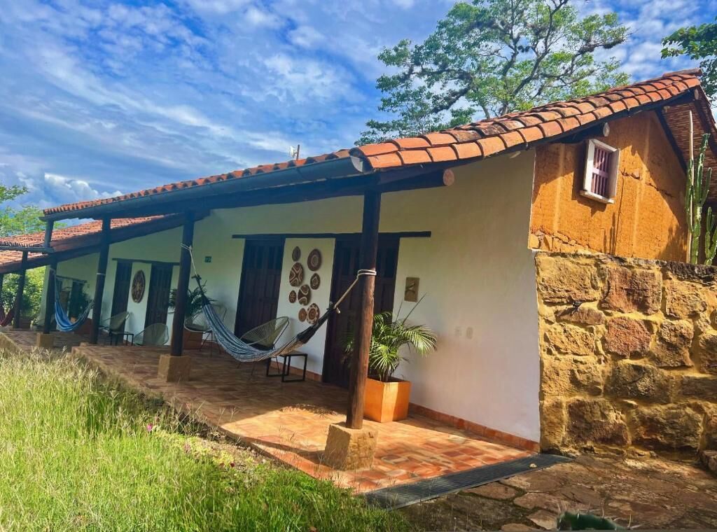 A traditional stone building with a tiled roof, a covered patio area with hammocks, and a potted plant.