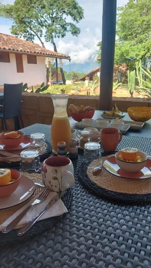A breakfast table set outdoors with various dishes, a bottle of juice, and a view of a rural landscape.