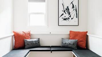 A room with a bench seat, a window, and a framed artwork on the wall.
