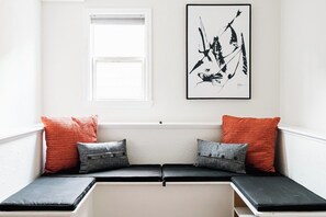 Una habitación con un banco, una ventana y una obra de arte enmarcada en la pared.