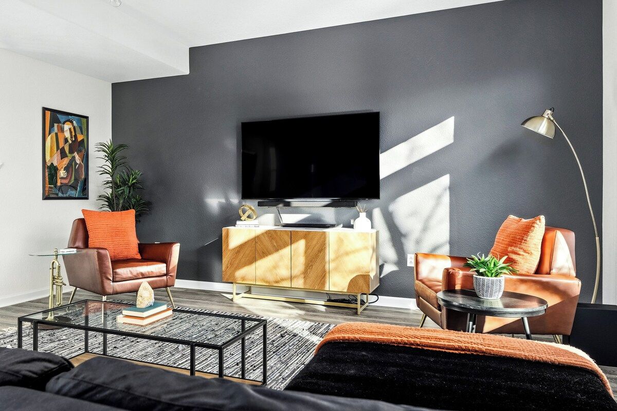 Ein modernes Wohnzimmer mit Flachbildfernseher, Ledersesseln, einem Couchtisch und einem Beistelltisch mit Pflanze.