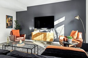 Una sala de estar moderna con un televisor de pantalla plana, sillones de cuero, una mesa de centro y una mesita auxiliar con una planta.