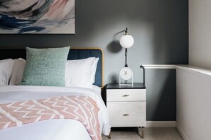 A neatly made bed with a patterned blanket, a bedside table with a lamp, and a painting on the wall.