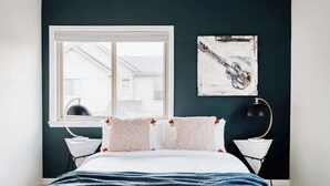 Ein Schlafzimmer mit großem Fenster, einem Bett mit weißer Bettwäsche, zwei Nachttischen und einer Wandlampe.