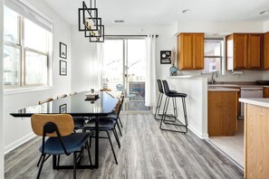 Una cocina moderna con armarios de madera, un comedor con mesa de vidrio y vistas a través de un ventanal corredero.