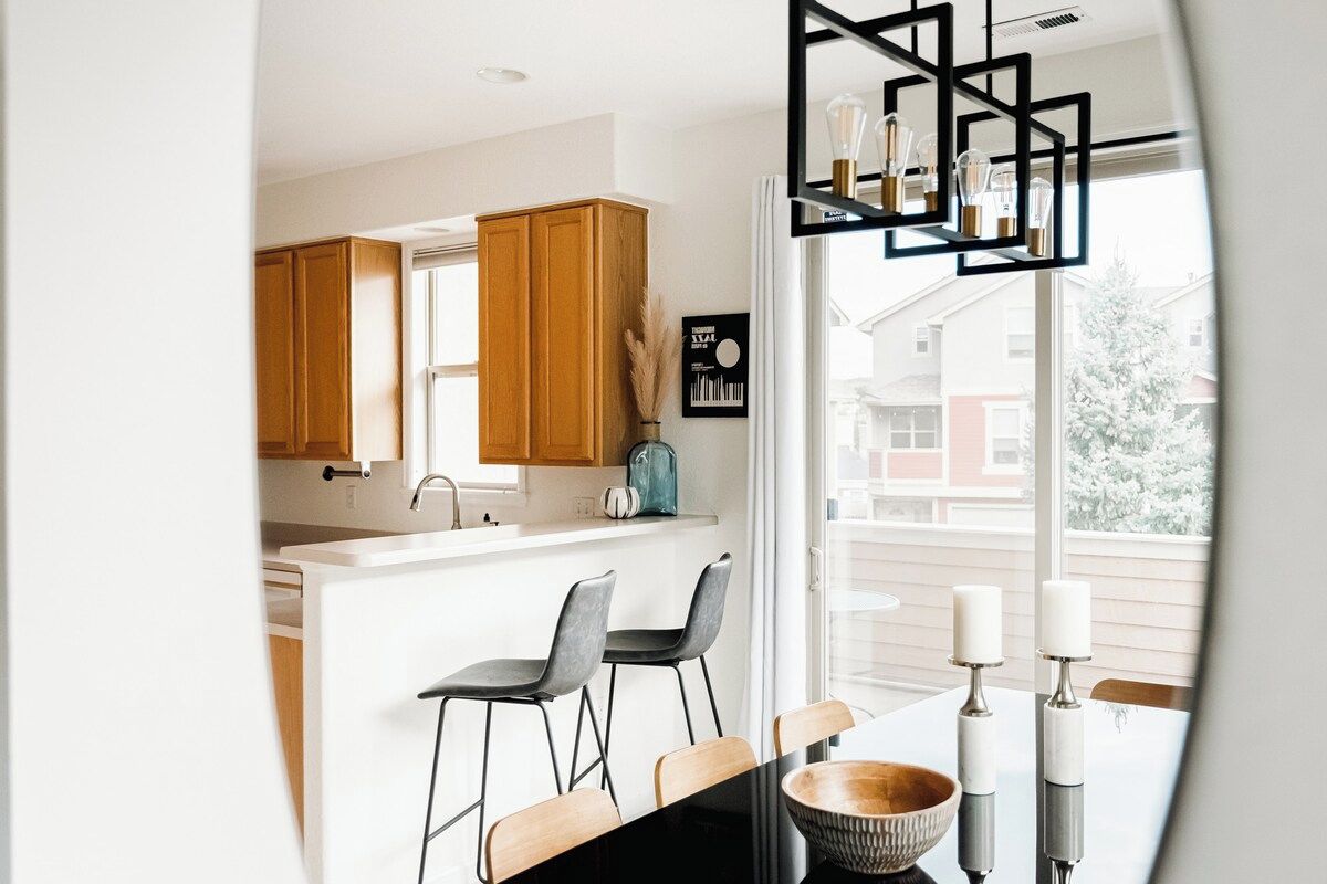 Une cuisine moderne avec des meubles en bois, un plan de travail blanc et un coin repas comprenant des tabourets de bar et une table.