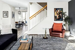 A modern living room with a staircase, a leather armchair, a coffee table, and a dining area in the background.