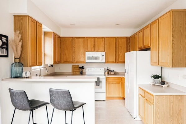Una cocina moderna con armarios de madera, una isla central con taburetes de bar, un microondas y un refrigerador.