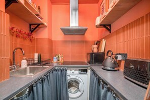 A compact kitchen with a washing machine, microwave, and kettle. - Charming studio flat near Notting Hill (London)