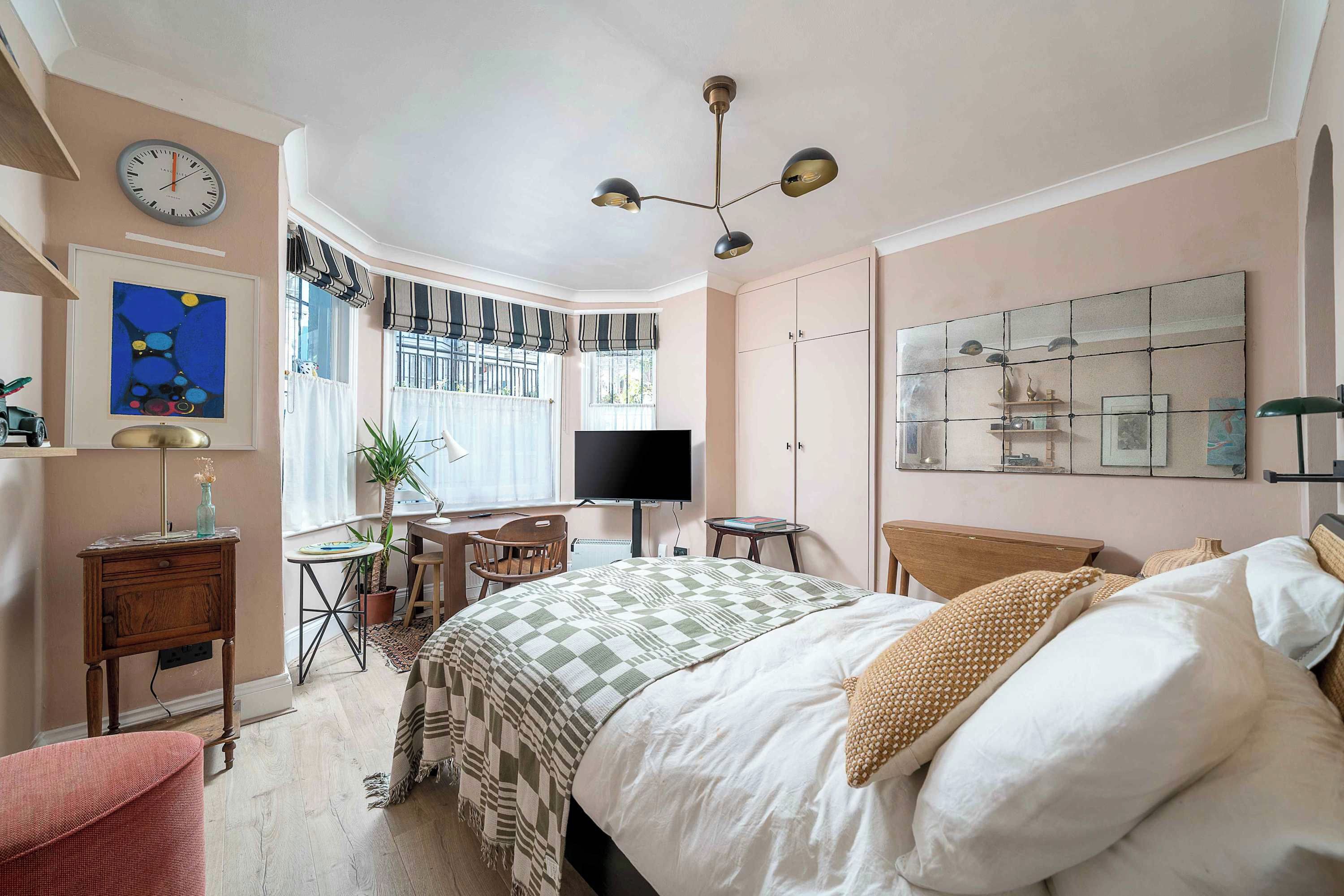 A bedroom with a bed, a desk, a chair, a television, and a large window with curtains.