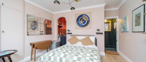 A bedroom with a checkered bedspread, a desk, a chair, a mirror, and a ceiling light fixture.
