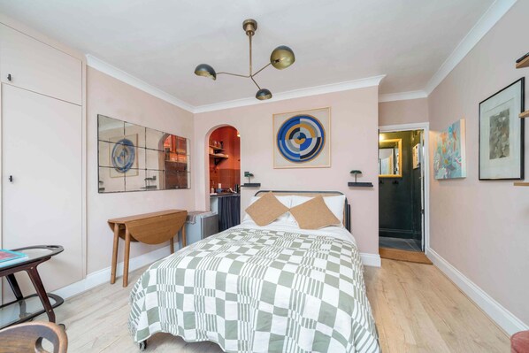 A bedroom with a checkered bedspread, a desk, a chair, a mirror, and a ceiling light fixture.