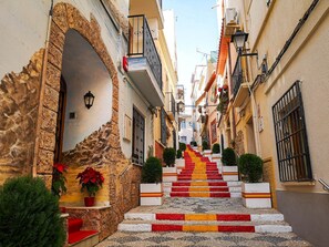 A narrow street with a stone archway, a staircase with red and yellow steps, and buildings with balconies and windows.