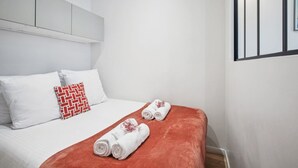 A hotel room with a bed, two pillows, a red throw blanket, and two rolled towels. - Central Bordeaux Gem AC Jacuzzi (Bordeaux)
