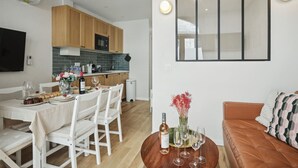 A modern kitchen with wooden cabinets, a dining table set for four, and a living area with a sofa and a coffee table. - Central Bordeaux Gem AC Jacuzzi (Bordeaux)