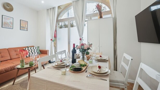A dining area with a table set for four, a sofa, and a TV mounted on the wall. - Central Bordeaux Gem AC Jacuzzi (Bordeaux)