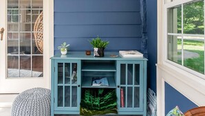 Una habitación con una pared azul acento, un aparador azul verdoso con puertas de vidrio, un tapete estampado y un banco de madera.