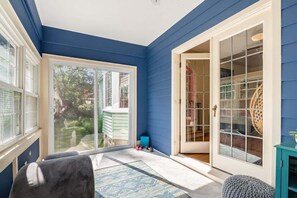Una habitación con una pared exterior azul, un portón corredizo de vidrio que da a un jardín y una alfombra pequeña en el suelo.