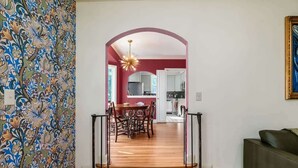 Un interior moderno con una escalera de madera que conduce a un comedor, una cocina visible a través de un arco, y un sofá verde en primer plano.