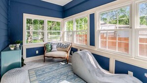 Una habitación con ventanas amplias, pared azul, un banco acolchado y una alfombra estampada.