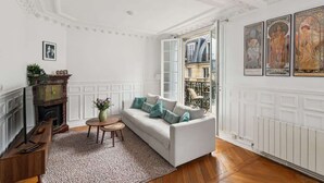 Una sala de estar con un sofá blanco, una chimenea, una mesa de centro de madera y vistas a través de un ventanal abierto.