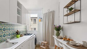 Cocina compacta con armarios blancos, salpicadero de azulejos, un taburete pequeño y una zona para desayunar sobre la encimera.