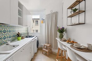 Una cucina compatta con mobili bianchi, zoccolo in piastrelle, un piccolo sgabello e angolo colazione sul bancone.