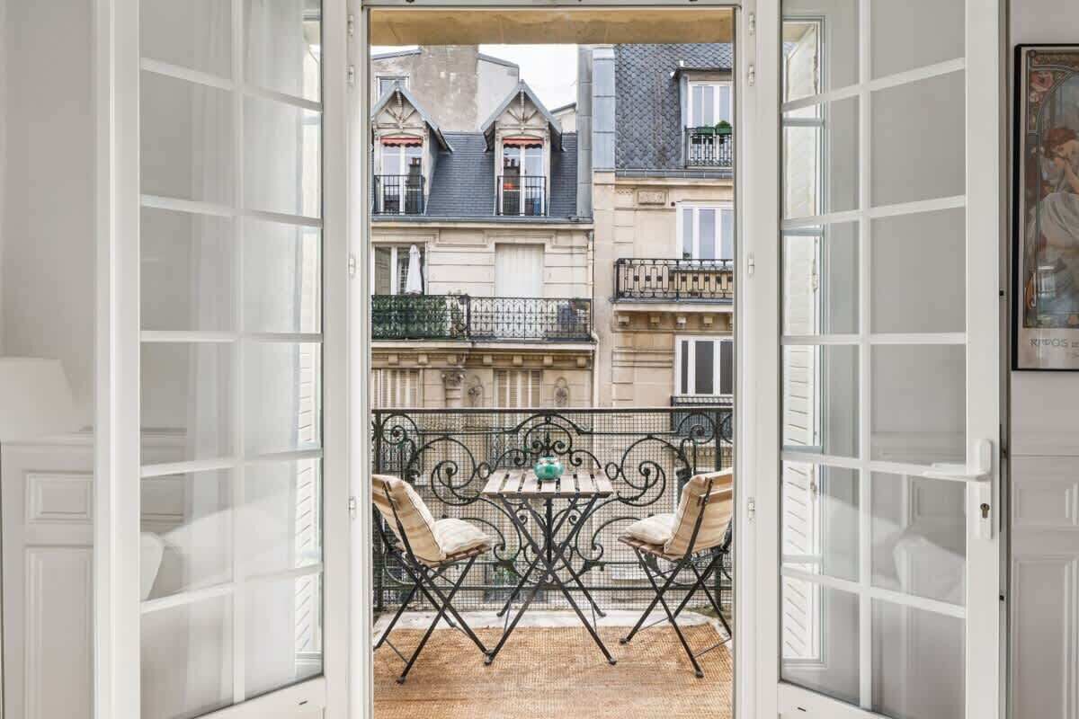 An open balcony with a table and chairs, overlooking a row of buildings with balconies.