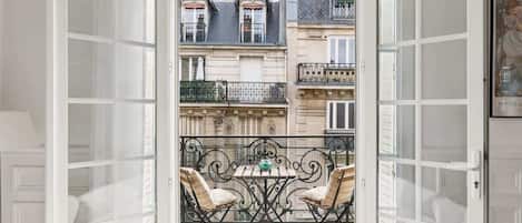 An open balcony with a table and chairs, overlooking a row of buildings with balconies.