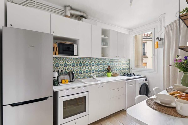 A compact kitchen with white cabinetry, a built-in microwave, a stove, and a washing machine.