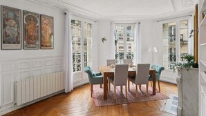 Un comedor con mesa y sillas de madera, un radiador y vistas amplias a través de grandes ventanales.