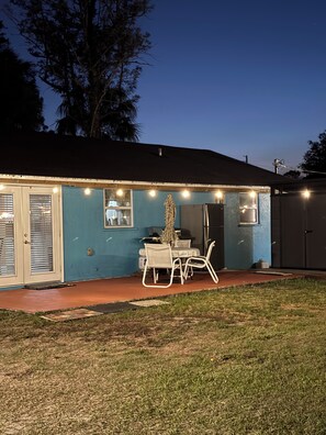 A house with a blue exterior, a patio with a table and chairs, and string lights along the roofline.