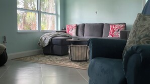 A living room with a blue sofa, a grey couch, and a drum set. There is a large window with a view of trees. - Chill  Cottage in charming Punta Gorda (Punta Gorda)