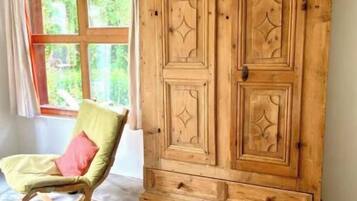 Ein Zimmer mit großem Holzschrank, Schaukelstuhl und einem fenster mit Vorhängen.