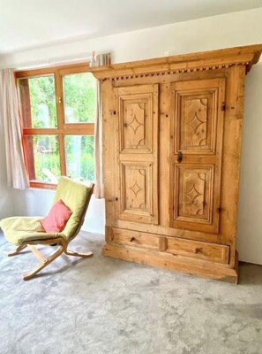 A room with a large wooden wardrobe, a rocking chair, and a window with curtains.