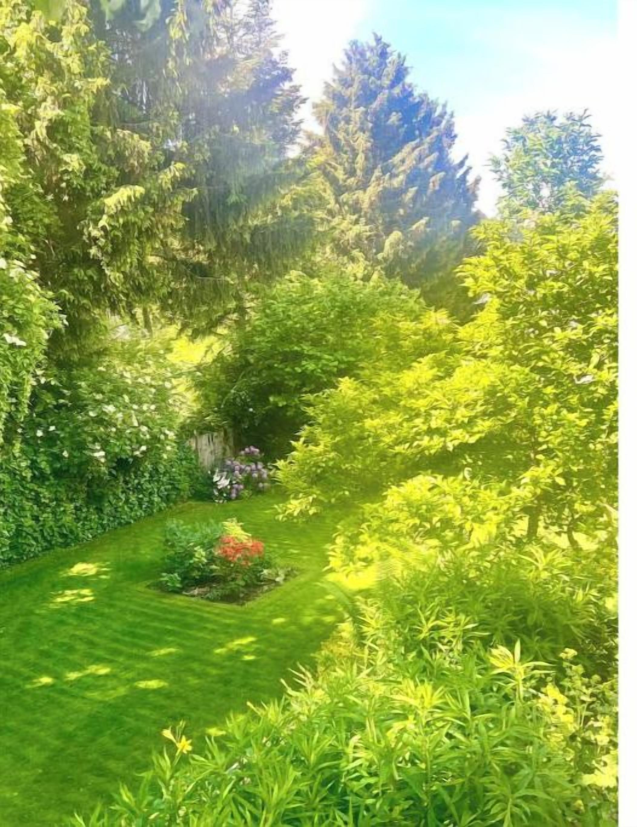 Ein üppiger Garten mit vielfältigen Pflanzen und Bäumen, einem gepflegten Rasen und einem kleinen Blumenbeet.