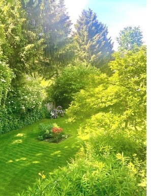 Un jardin luxuriant, avec une grande variété de plantes et d’arbres, une pelouse bien entretenue et un petit parterre de fleurs.
